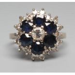 A SAPPHIRE AND DIAMOND CLUSTER RING, the central round brilliant cut diamond in a border of six claw