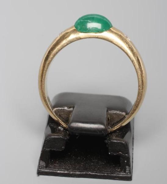 AN EMERALD AND DIAMOND RING, the oval cabochon polished emerald tension set and flanked by two gypsy - Bild 2 aus 3