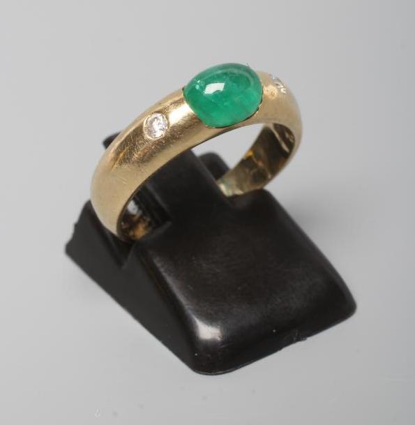 AN EMERALD AND DIAMOND RING, the oval cabochon polished emerald tension set and flanked by two gypsy