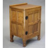 A ROBERT THOMPSON ADZED OAK BEDSIDE CABINET of canted multi-panelled oblong form, the moulded