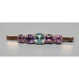 AN EDWARDIAN BROOCH centred by a cushion cut blue zircon flanked by two pairs of graduated amethysts