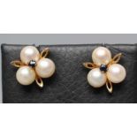 A PAIR OF CULTURED PEARL EAR STUDS, the three pearls peg set and centred by a small sapphire with