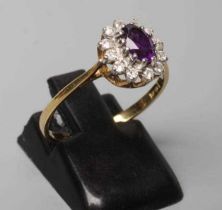 AN AMETHYST AND DIAMOND CLUSTER RING, the oval facet cut amethyst claw set to a border of small