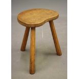 ALBERT JEFFRAY, AN ADZED OAK STOOL, of kidney form raised on three faceted splayed legs, incised