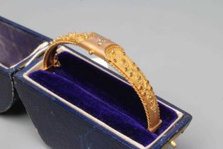 A 9CT GOLD STIFF HINGED BANGLE, the upper section gypsy set with a trefoil of three small diamonds