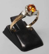 AN ORANGE SAPPHIRE AND DIAMOND THREE STONE RING, the round facet cut sapphire claw set and flanked