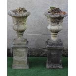 A PAIR OF CAST STONE URNS of half fluted campana form with ovolu moulded rim, a band of foliate