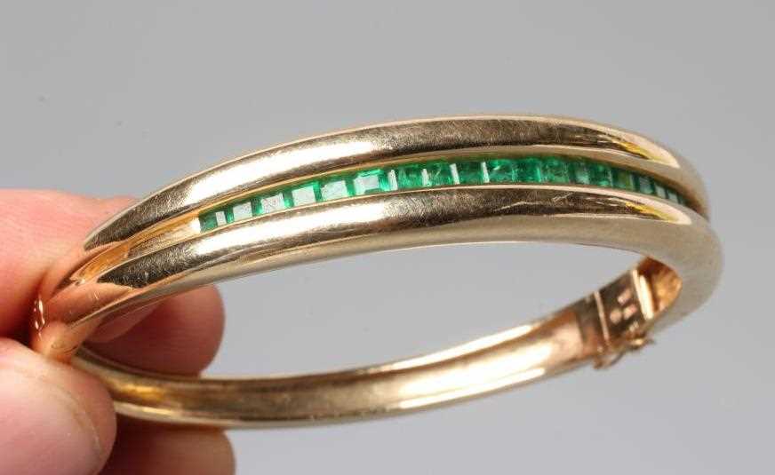 AN EMERALD STIFF HINGED BANGLE, the upper section channel set with twenty two graduated calibre - Image 2 of 3