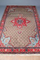 A PERSIAN RUG, the camel trellis patterned field with central crimson gul and pale blue spandrels,