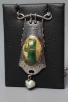 A MURRLE BENNETT PENDANT, the mottled cream and green glass oval cabochon in a planished shaped