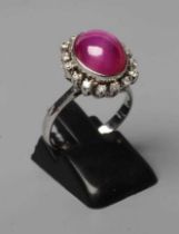 A STAR RUBY AND DIAMOND RING, the oval cabochon ruby collet set to a border of sixteen small