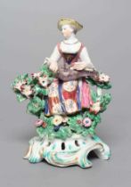 A BOW PORCELAIN FIGURE, c.1760, modelled as Columbine, seated and wearing colourful clothing,