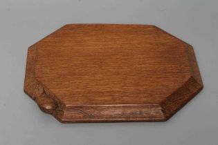 A ROBERT THOMPSON ADZED OAK BREAD BOARD of canted oblong form, the moulded edge with carved mouse