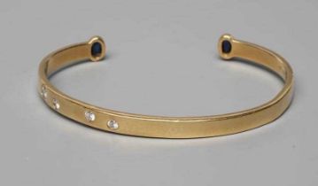 A BANGLE, stamped 750, asymetrically set with four graduated round brilliant cut stones, each
