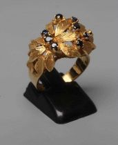 A COCKTAIL RING, the high flowerhead panel claw set with nine small sapphires to a plain wide