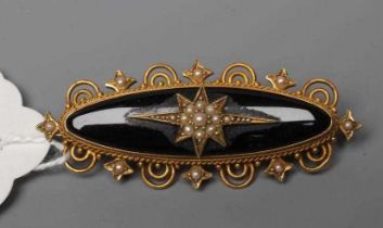 A VICTORIAN MOURNING BROOCH, the eliptical black panel centred by a gypsy set and seed pearl star,
