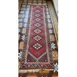 A vintage wool carpet runner in shades of red. 288 l x 82cm w without tassels.