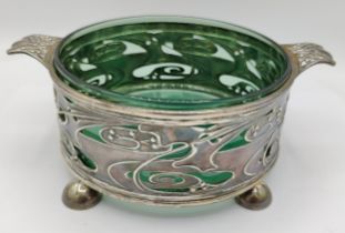 A silver Art Nouveau twin handle bowl with green glass liner raised on feet, hallmarked London 1900