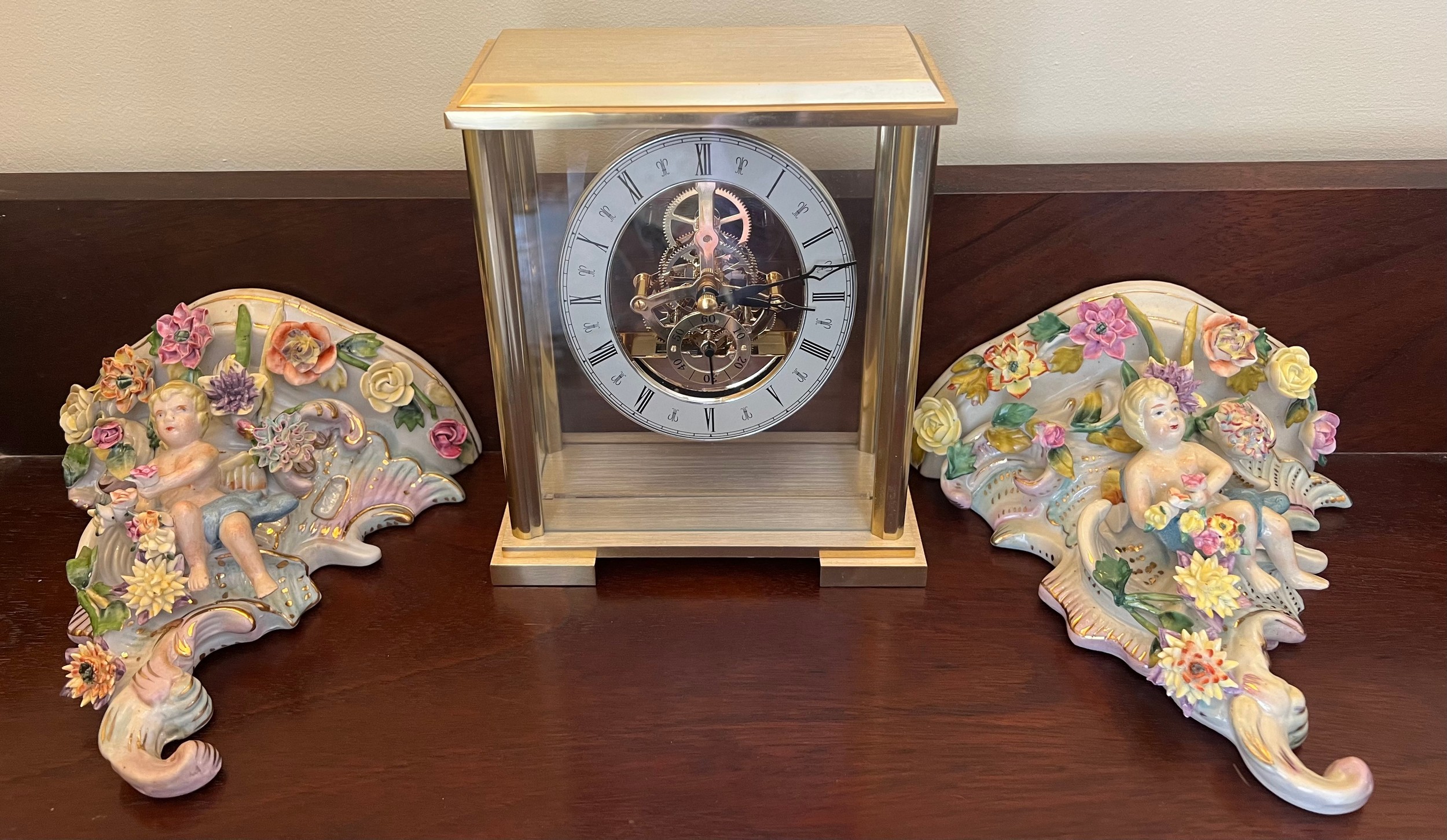 A modern gilt cased mantle clock together with two continental porcelain wall brackets with putti