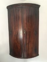 A Georgian mahogany two door corner cupboard with shelves and three small drawers to the interior.