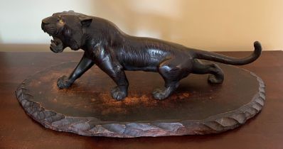 A Meiji period Japanese bronze tiger with glass eyes on wooden stand. 30cm l . Marked to underside