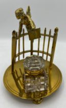 A 19thC brass inkstand and brass mounted glass inkwell formed as a cherub leaning over a fence