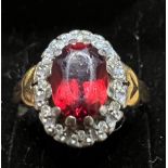 An 18 carat gold ring set with red stone surrounded by diamonds. Size M. Weight 4.2gm.