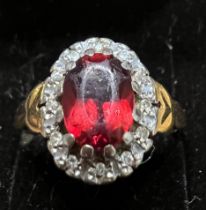 An 18 carat gold ring set with red stone surrounded by diamonds. Size M. Weight 4.2gm.