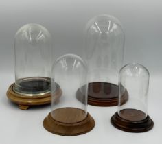 Four glass domes on wooden bases, varying sizes. Tallest 27.5cm, shortest 15cm approx.