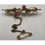 A 15 carat gold bar brooch set with seed pearl and rubies with safety chain. 2.6gm.