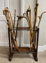A wooden umbrella stick stand containing a selection of wooden walking sticks, one stick with