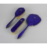 A George V silver and blue enamel three piece dressing table set of hand mirror and two brushes,