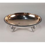 An American sterling silver oval dish with gilt interior and gadrooned border, on four rams head