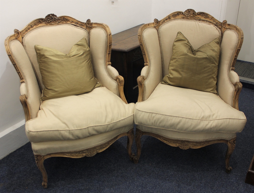 A pair of Louis XV style cream upholstered armchairs, with floral carved frames, on slender cabriole