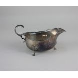 A George VI silver sauce boat with flying scroll handle on three shell capped hoof feet, Chester