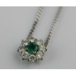 An emerald and diamond nine stone cluster pendant claw set with the circular cut emerald at the