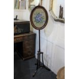 A Victorian pole screen with glazed oval needlework panel on outswept tripod legs