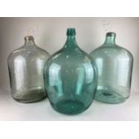A large green glass bottle and two wine demi johns, height 50cm
