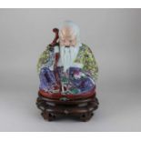 A Chinese porcelain figure of Shou-Lao seated on a low chair, holding peach and staff, impressed