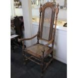 A baronial style carved high back chair with cane seat and back, scroll handles on block and