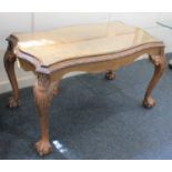 A reproduction walnut coffee table with rectangular serpentine top and glass cover on scroll