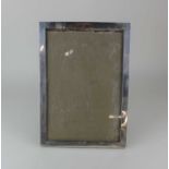 A George V silver photograph frame with plain rectangular border, wooden back and stand, maker