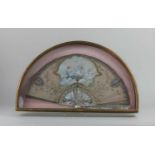 A framed painted and sequinned fan decorated with a classical figure, birds and cherubs, the