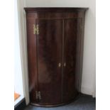 A George III mahogany bowfront corner cupboard with two doors and fancy scroll shaped H hinges