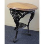 A cast iron patio table, with circular wooden top on cast iron mask capped tripod legs with
