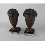 A pair of Art Deco patinated metal clock garniture vase ornaments, both with floral surmount, on