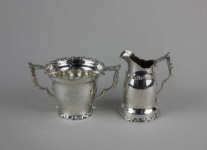 A sterling possibly American silver cream jug and sugar bowl with scroll decorated borders, engraved