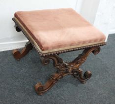 A Victorian carved stool with upholstered seat on scrolling X-frame supports