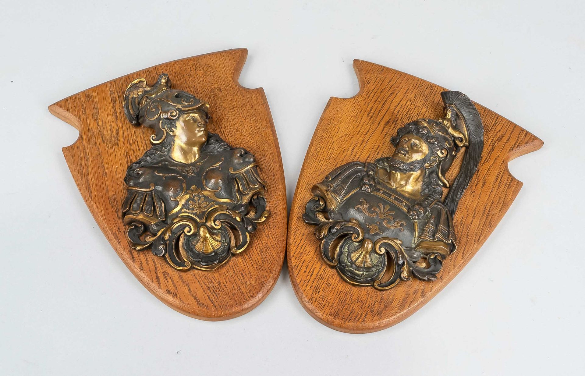 Pair of appliques, 19th/20th c., bronzed and patinated metal casting on crest-shaped oak plinth.