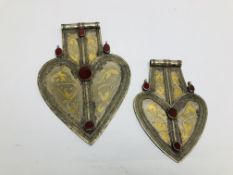 TWO EASTERN TRIBAL STYLE WHITE METAL HEART SHAPED PENDANTS WITH INSET OVAL STONE DETAIL.